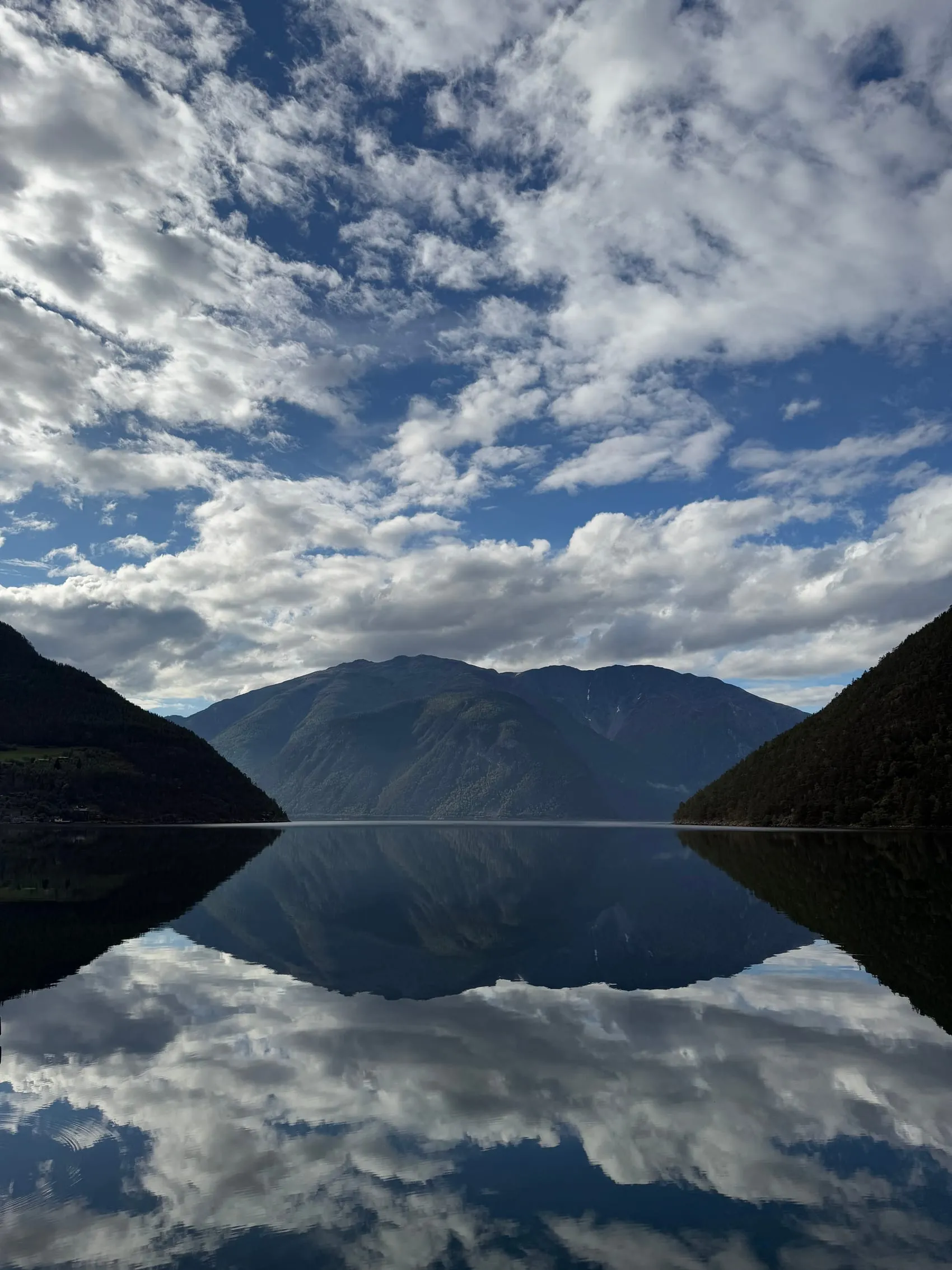 Fjellsidene speilet i den blikkstille fjorden.